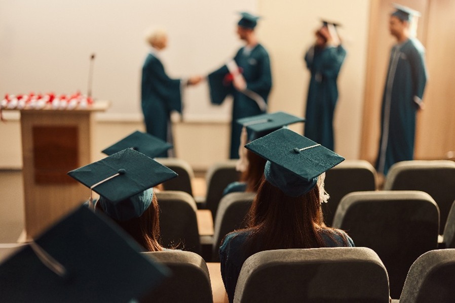 Fresno County reentry program graduation ceremony, view from behind seated graduates, with blurred graduates receiving diplomas and shaking hands with the program director.
