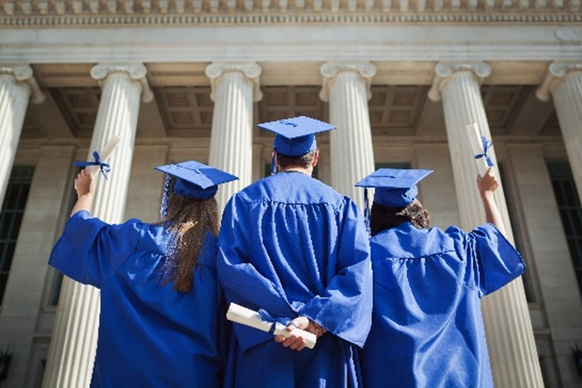 Two women and a man in caps and gowns standing in front of a government building, representing Luzerne County reentry program graduates
